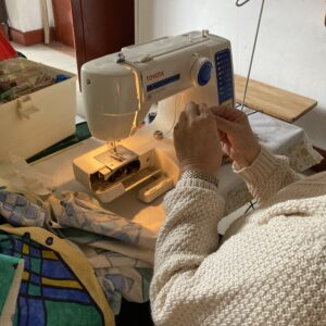 mains d'une personne assise devant une machine à coudre qui manipule du fil.