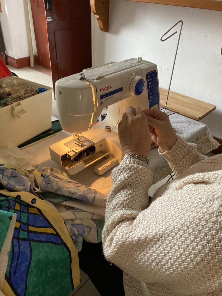 mains d'une personne assise devant une machine à coudre qui manipule du fil.