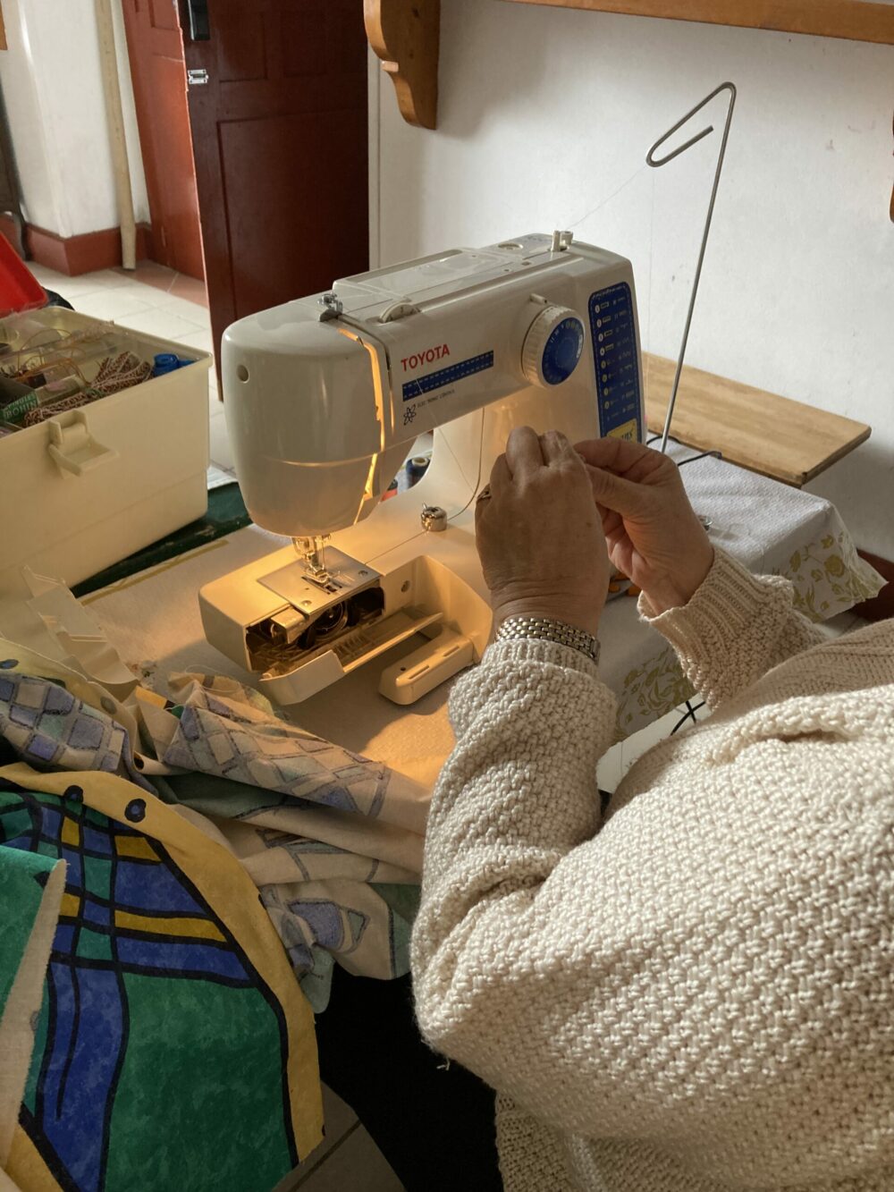 mains d'une personne assise devant une machine à coudre qui manipule du fil.