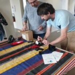 2 personnes concentrées, debout devant une table sur laquelle il y a différents outils de réparation.