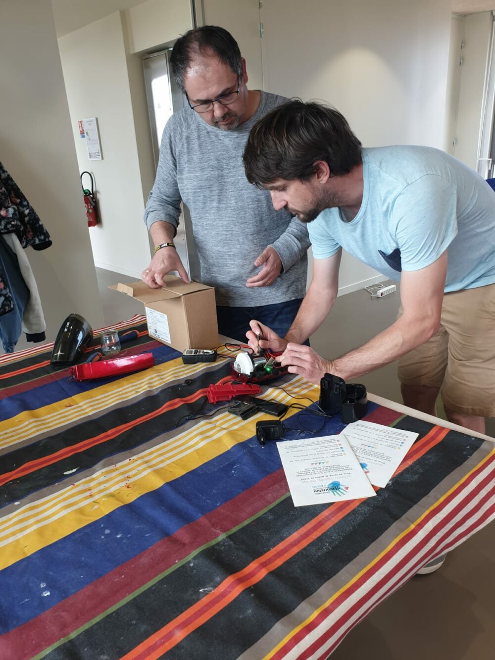 2 personnes concentrées, debout devant une table sur laquelle il y a différents outils de réparation.